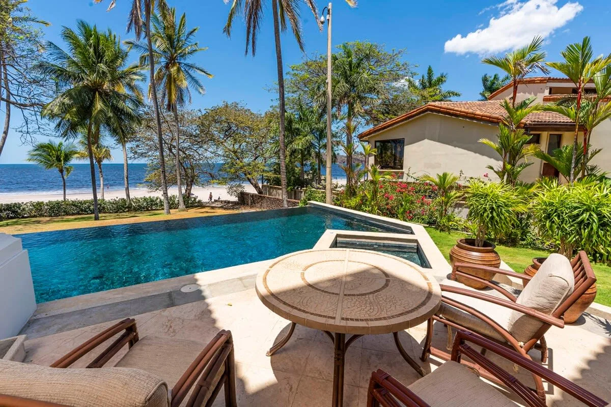 A poolside patio with outdoor seating overlooks a tropical beach.