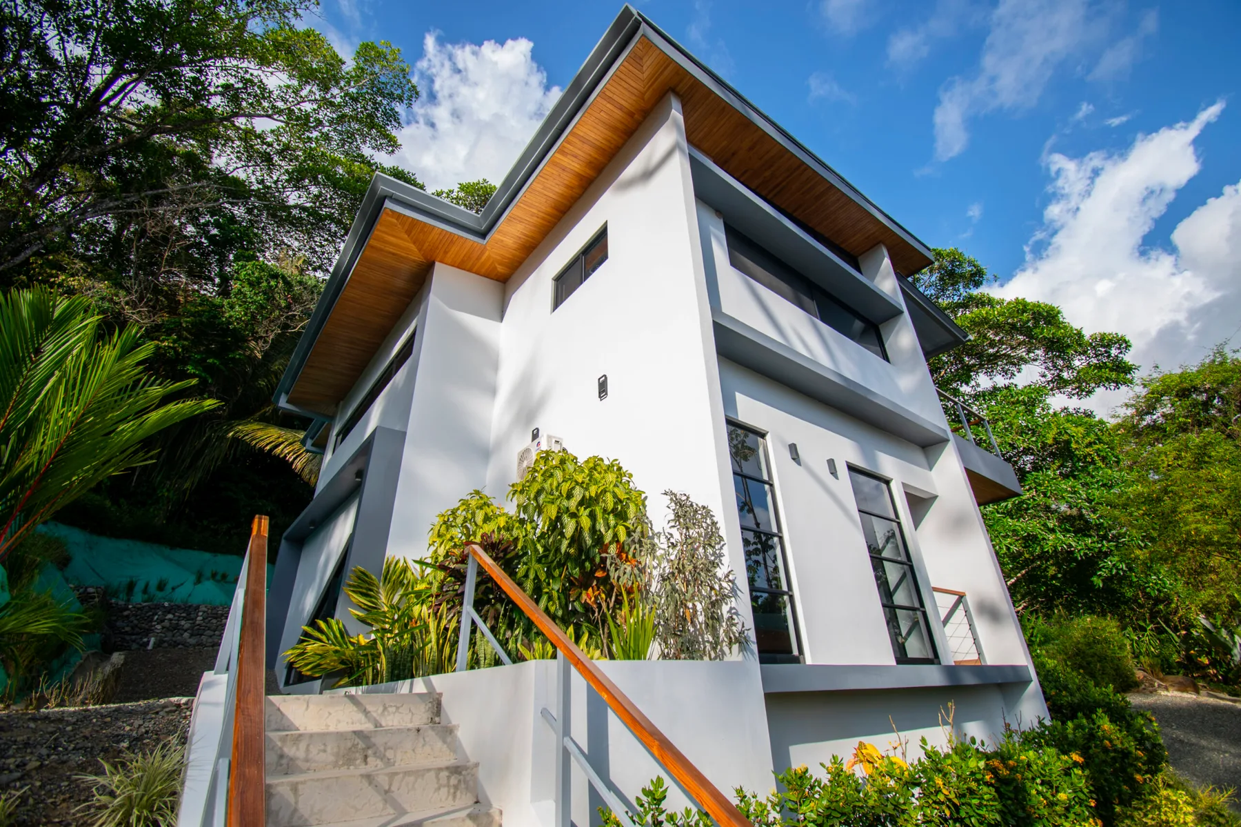A modern white house rises above an outdoor staircase surrounded by greenery.