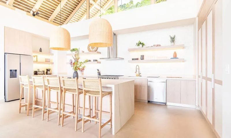 Casa Frenchie & Guest House · 15. A bright, open-plan kitchen features a vaulted beamed ceiling, a large island with bar seating, light wood cabinetry, and a high transom window offering jungle views.