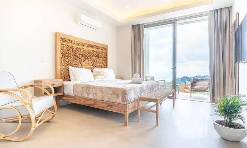 Casa Frenchie & Guest House · 33. This bright bedroom features a bed with a carved wooden headboard, opening through glass doors to a balcony offering ocean and jungle views.