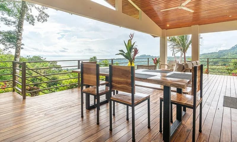 Casa Frenchie & Guest House · 18. A spacious covered wooden deck features a natural wood dining table and seating area, offering expansive views of the jungle and distant ocean.