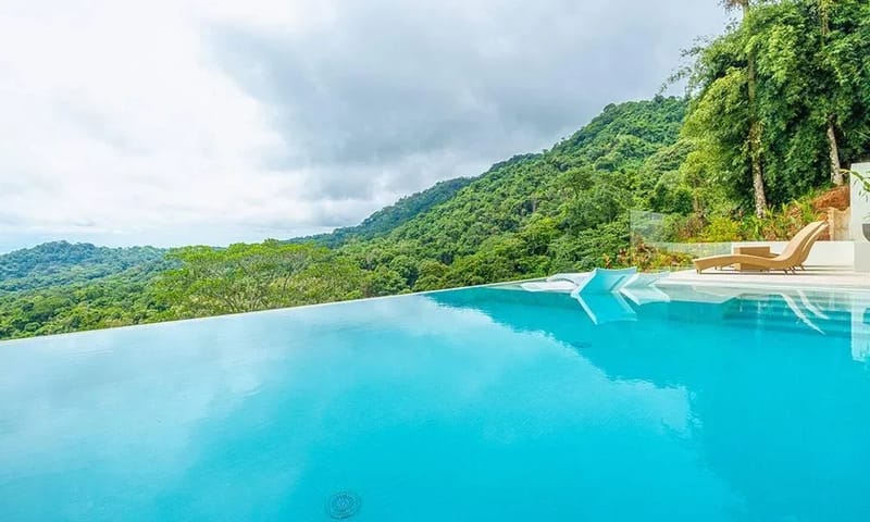 Casa Frenchie & Guest House · 22. The infinity pool overlooks dense jungle hills stretching to the horizon, with a bright pool deck and chaise loungers.