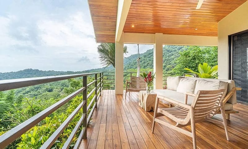 Casa Frenchie & Guest House · 29. A covered wooden terrace with a plank floor and ceiling hosts casual seating, opening to extensive views of the jungle-covered hills under natural light.