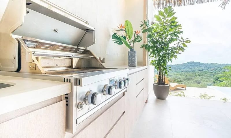 Casa Frenchie & Guest House · 16. A bright outdoor kitchen area, featuring a built-in stainless steel grill and light wood cabinetry, opens to extensive views of the tropical jungle.