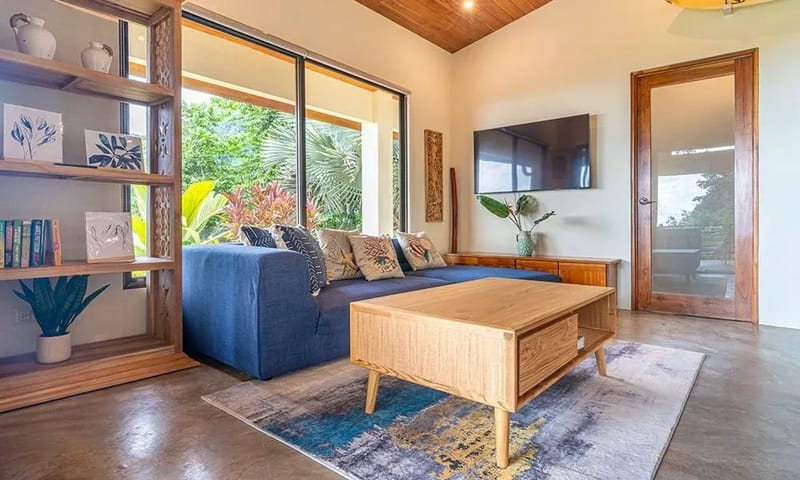 Casa Frenchie & Guest House · 8. This open living area features a vaulted wood ceiling, polished concrete floor, and expansive glass doors that open to a lush jungle view, filling the space with natural light.