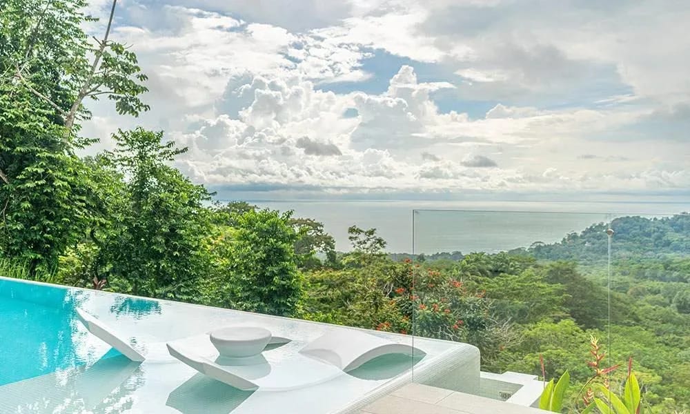 Casa Frenchie & Guest House · 1. The infinity pool features integrated submerged loungers and offers expansive views of the jungle and ocean under a bright, cloudy sky.