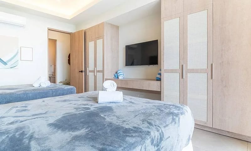 Casa Frenchie & Guest House · 12. This bright guest room features two queen beds, built-in light wood cabinetry with textured panels, a wall-mounted television, and an adjacent private bathroom.