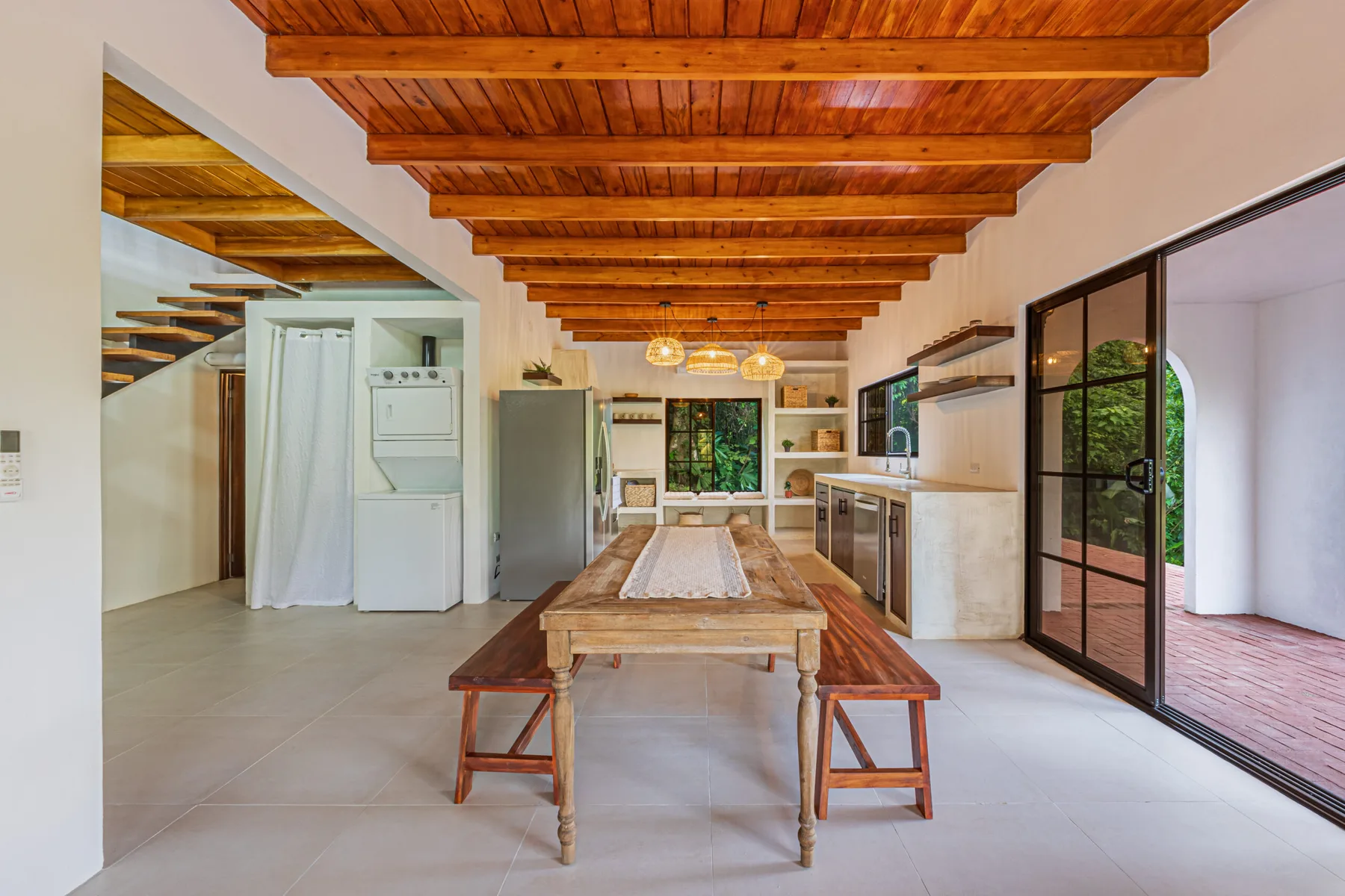 An open dining and kitchen area with a wooden table beneath exposed ceiling beams.