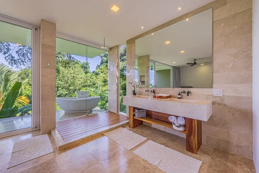 A bright bathroom with a long vanity, large mirror, and freestanding bathtub by the windows.