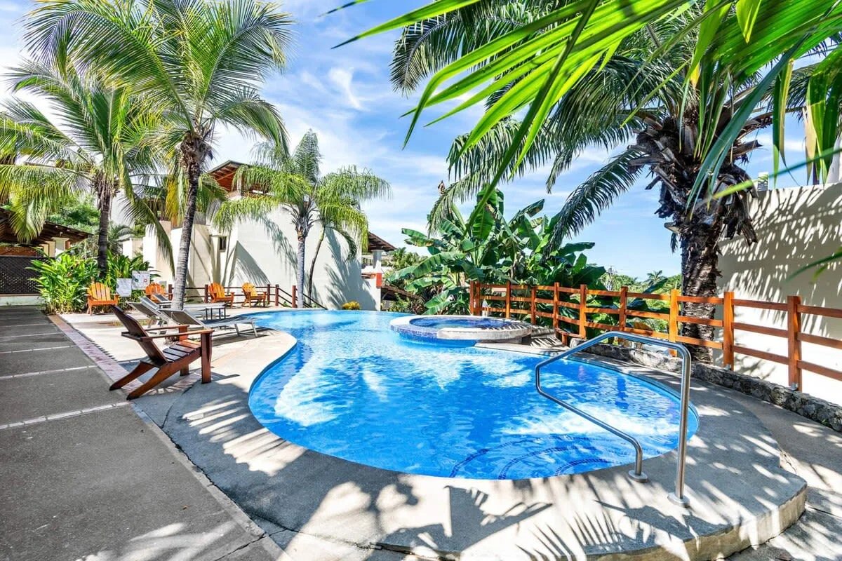 A swimming pool surrounded by palm trees, lounge seating, and a wooden railing.