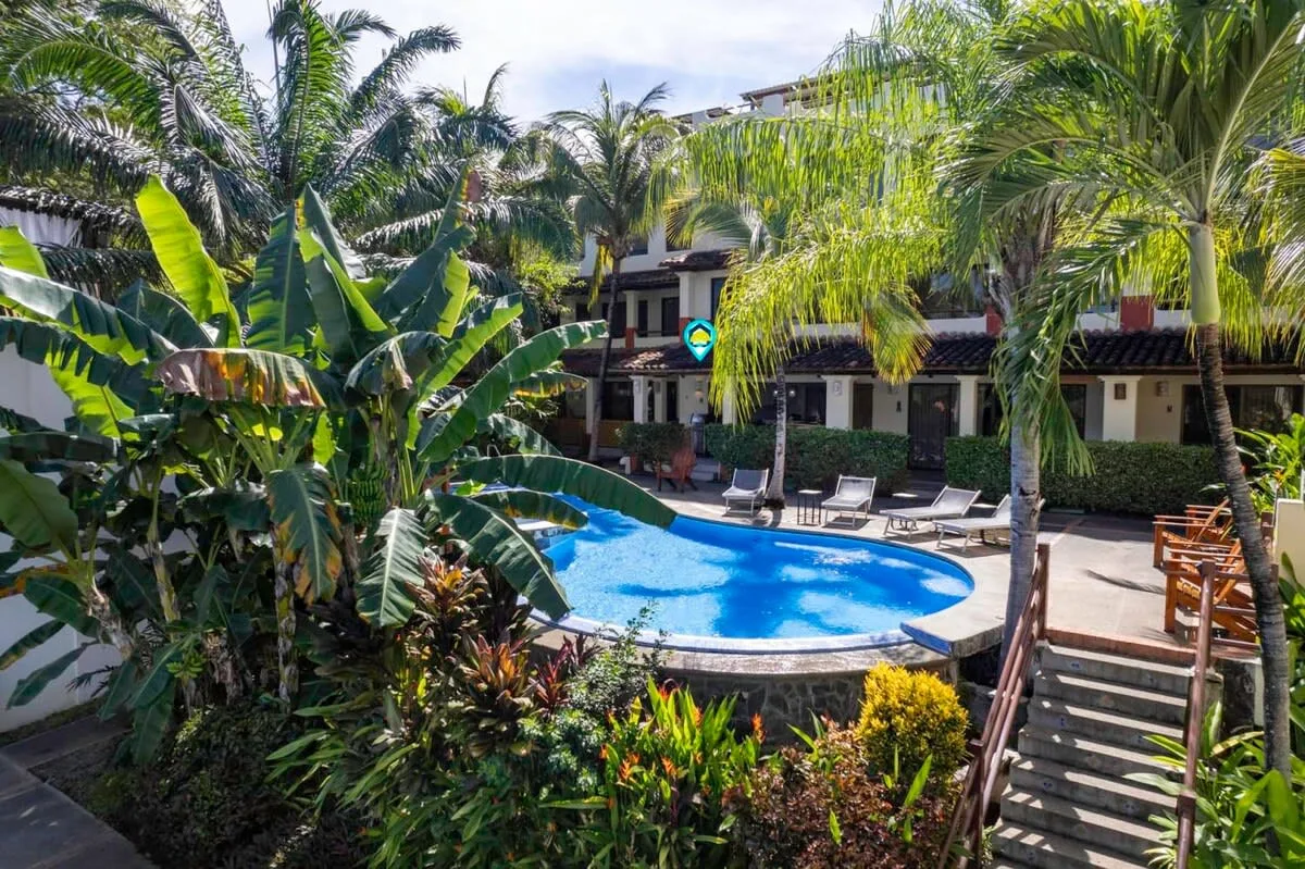 An outdoor swimming pool sits among lush tropical plants beside a building.