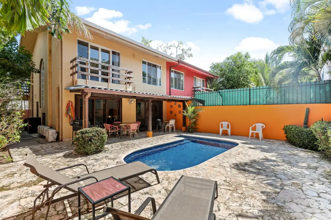 An outdoor pool patio beside a colorful building, with seating and surrounding greenery.