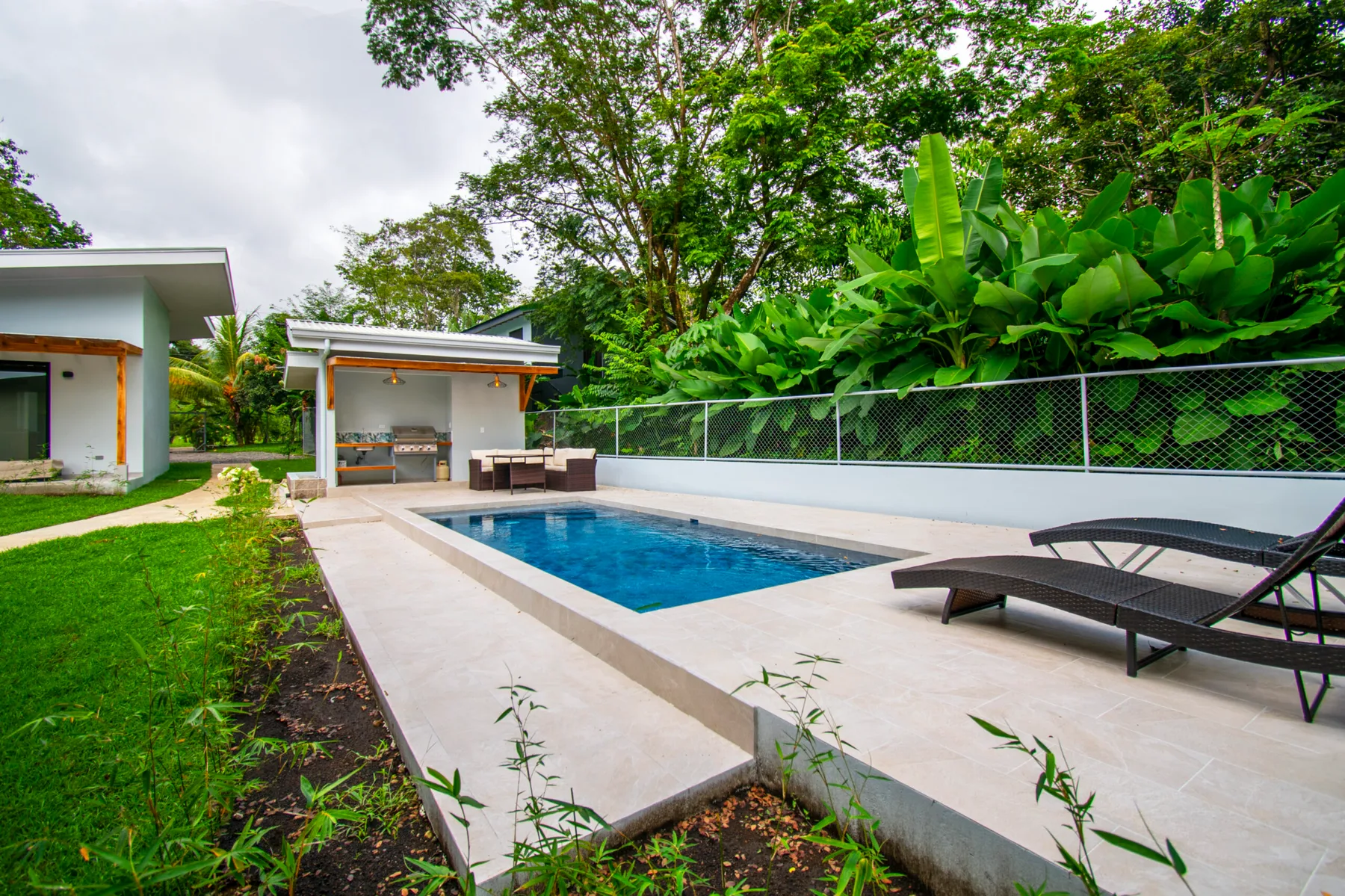 Una piscina al aire libre junto a un patio pavimentado y abundante vegetación tropical.