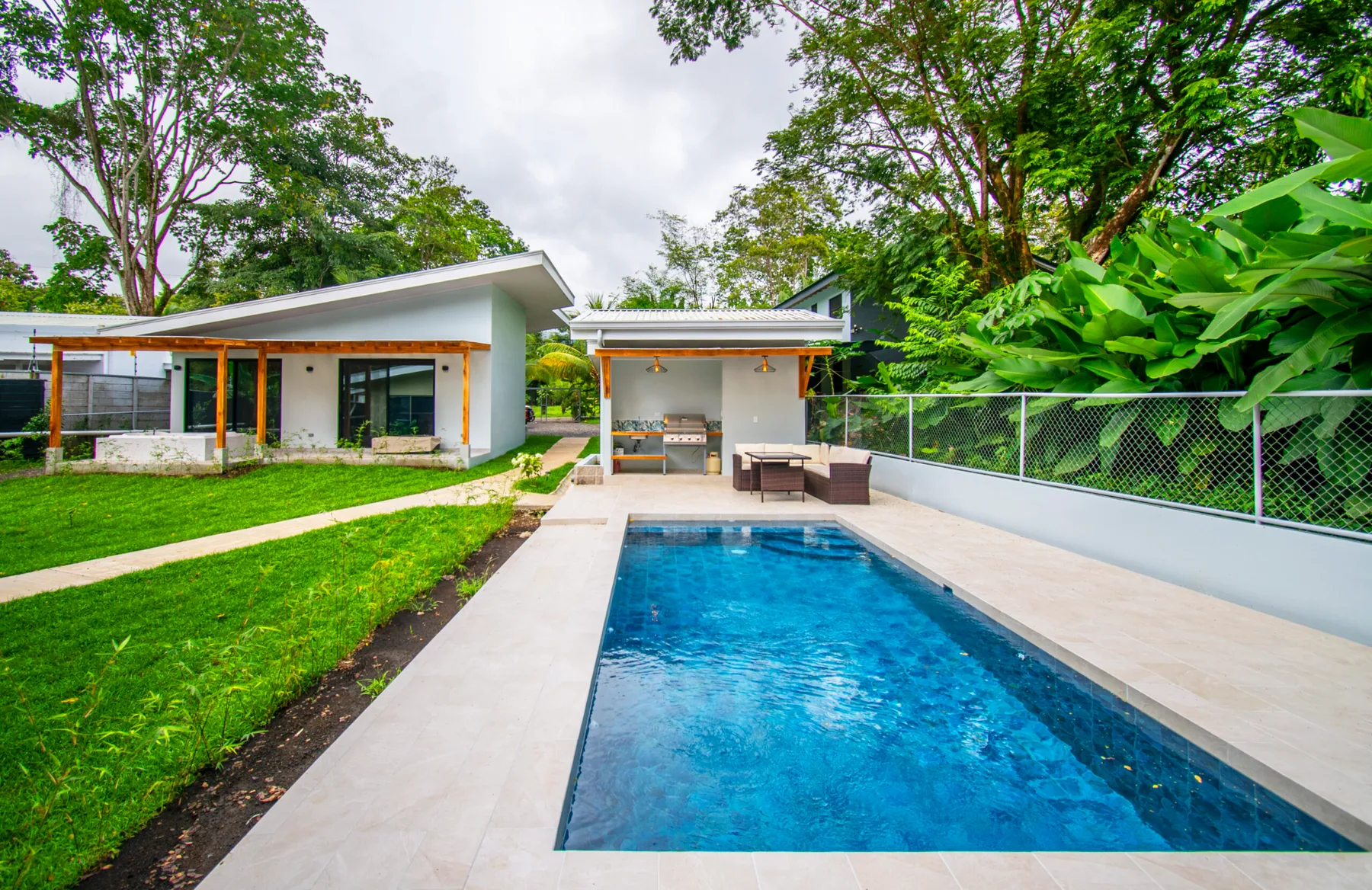 Una piscina al aire libre junto a una casa moderna y una zona de estar cubierta.