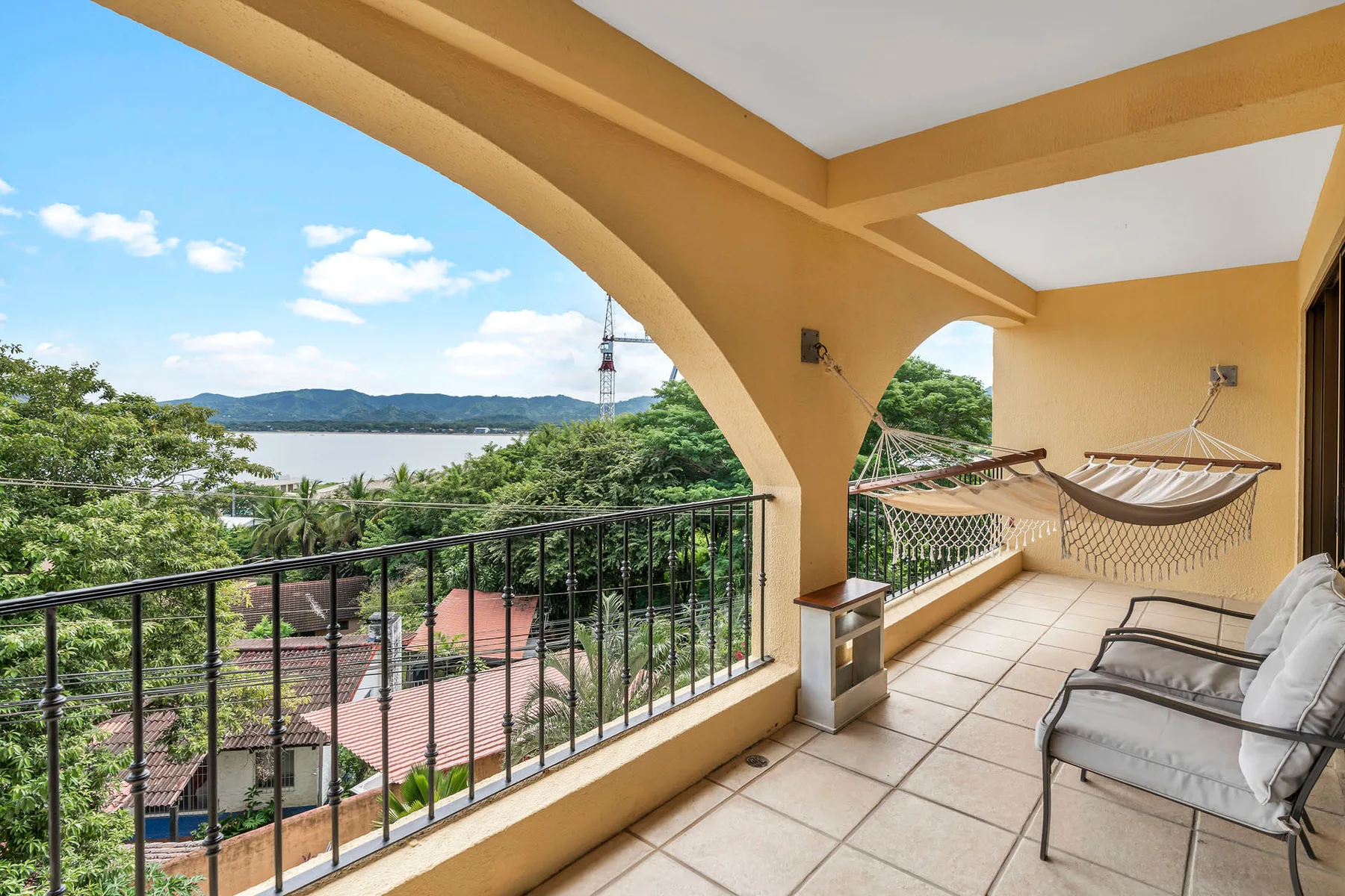 Una terraza cubierta mira hacia árboles, tejados y un lago, con asientos y una hamaca.