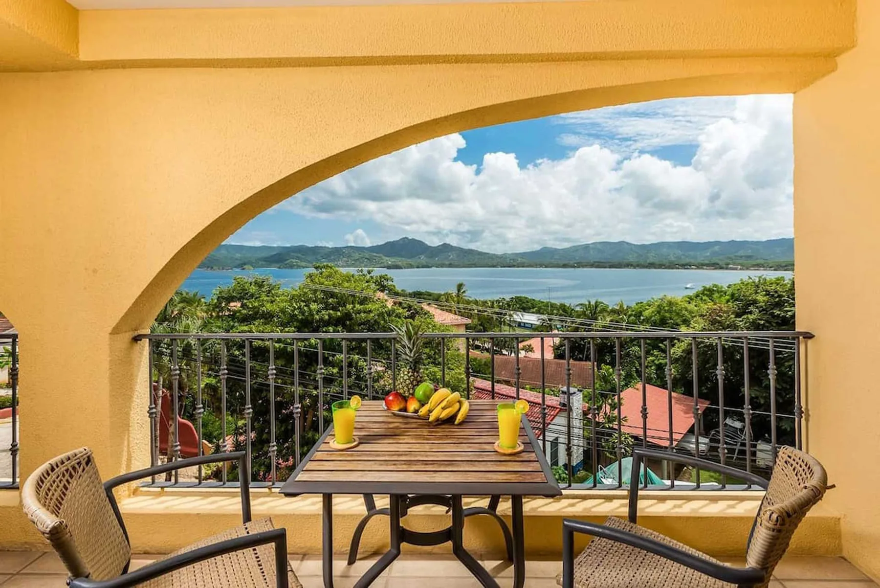 Un comedor en el balcón da a árboles frondosos, un lago y colinas lejanas.