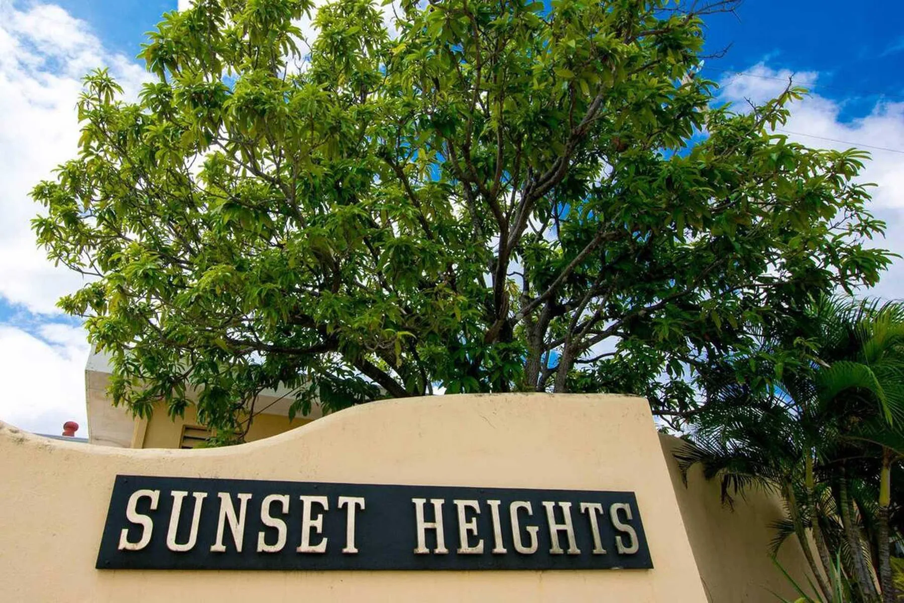 Un muro de entrada curvo muestra el nombre Sunset Heights bajo un árbol frondoso.
