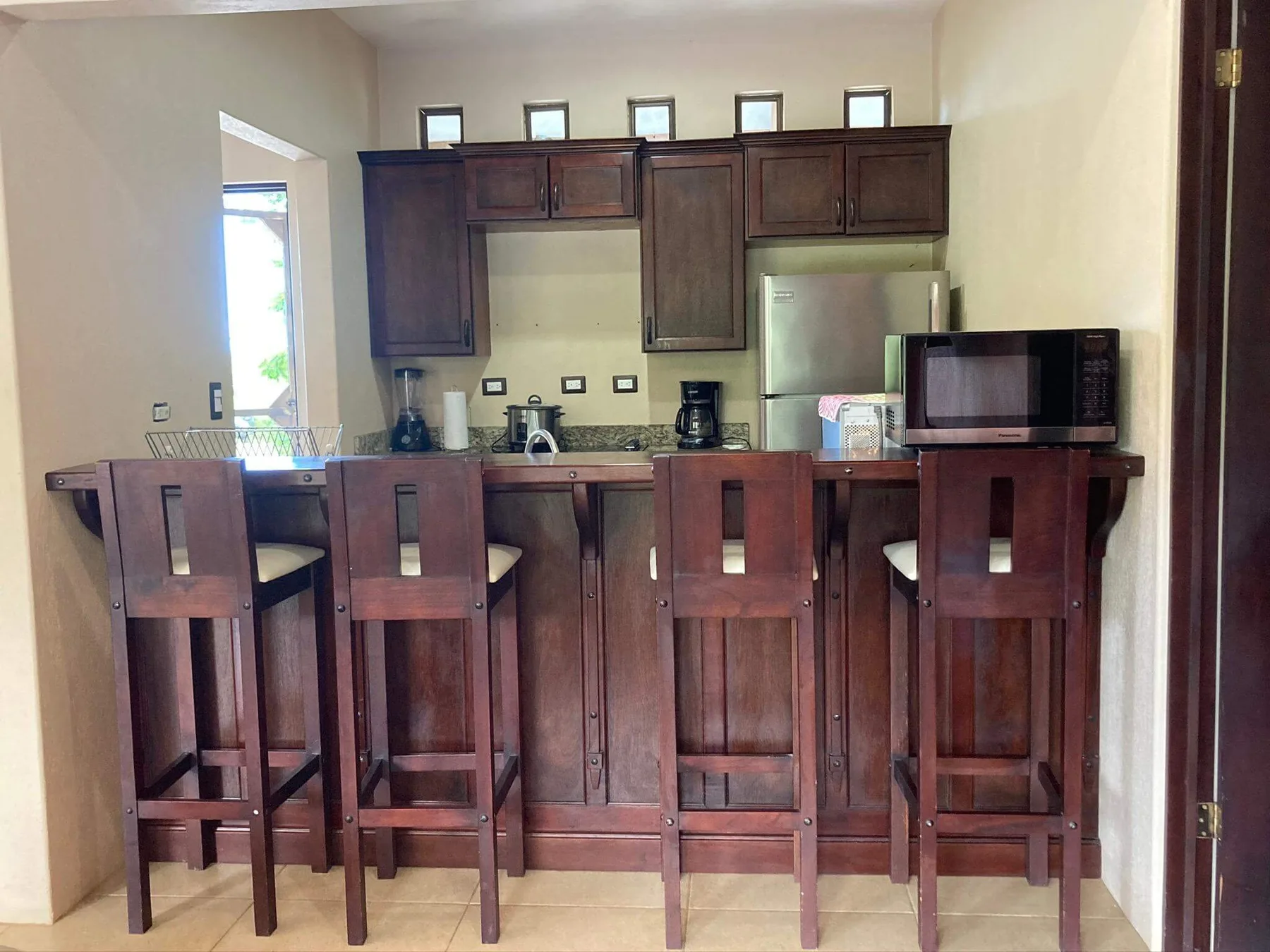 A kitchen with dark wooden cabinets and a counter lined with bar stools.