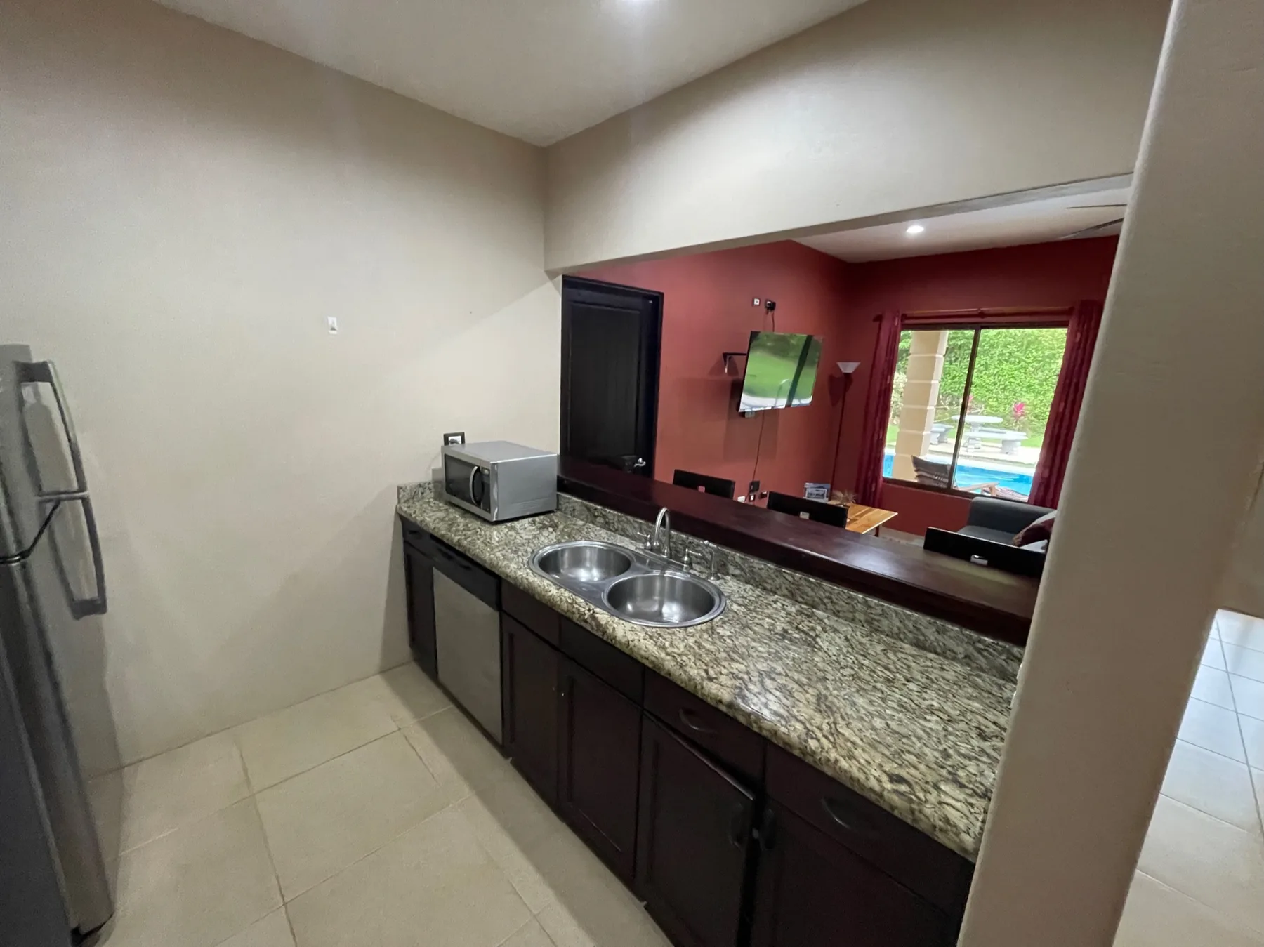 A kitchen counter with a sink and microwave faces a room with a television.