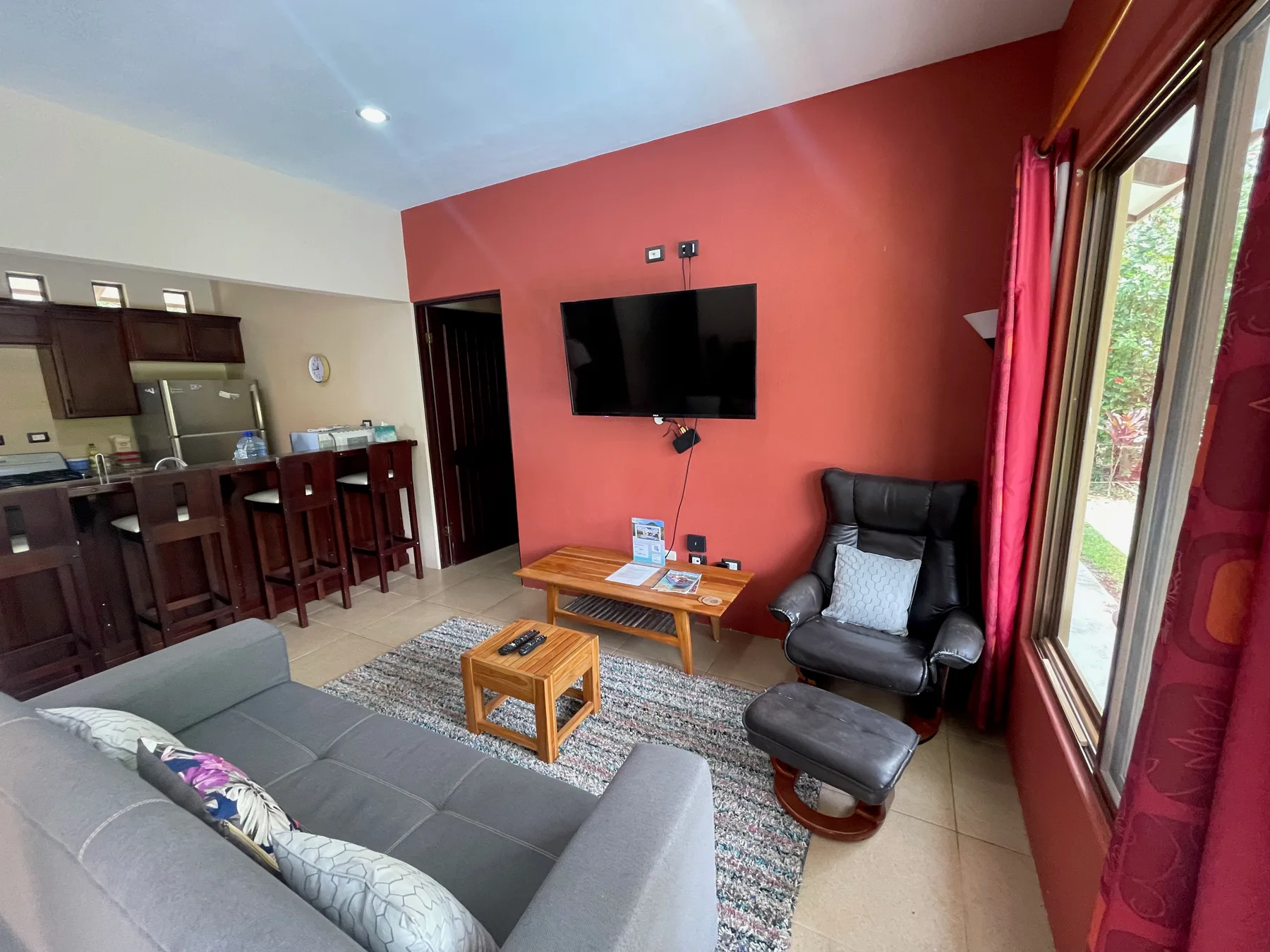 A living room with seating, a television, and an adjoining kitchen.