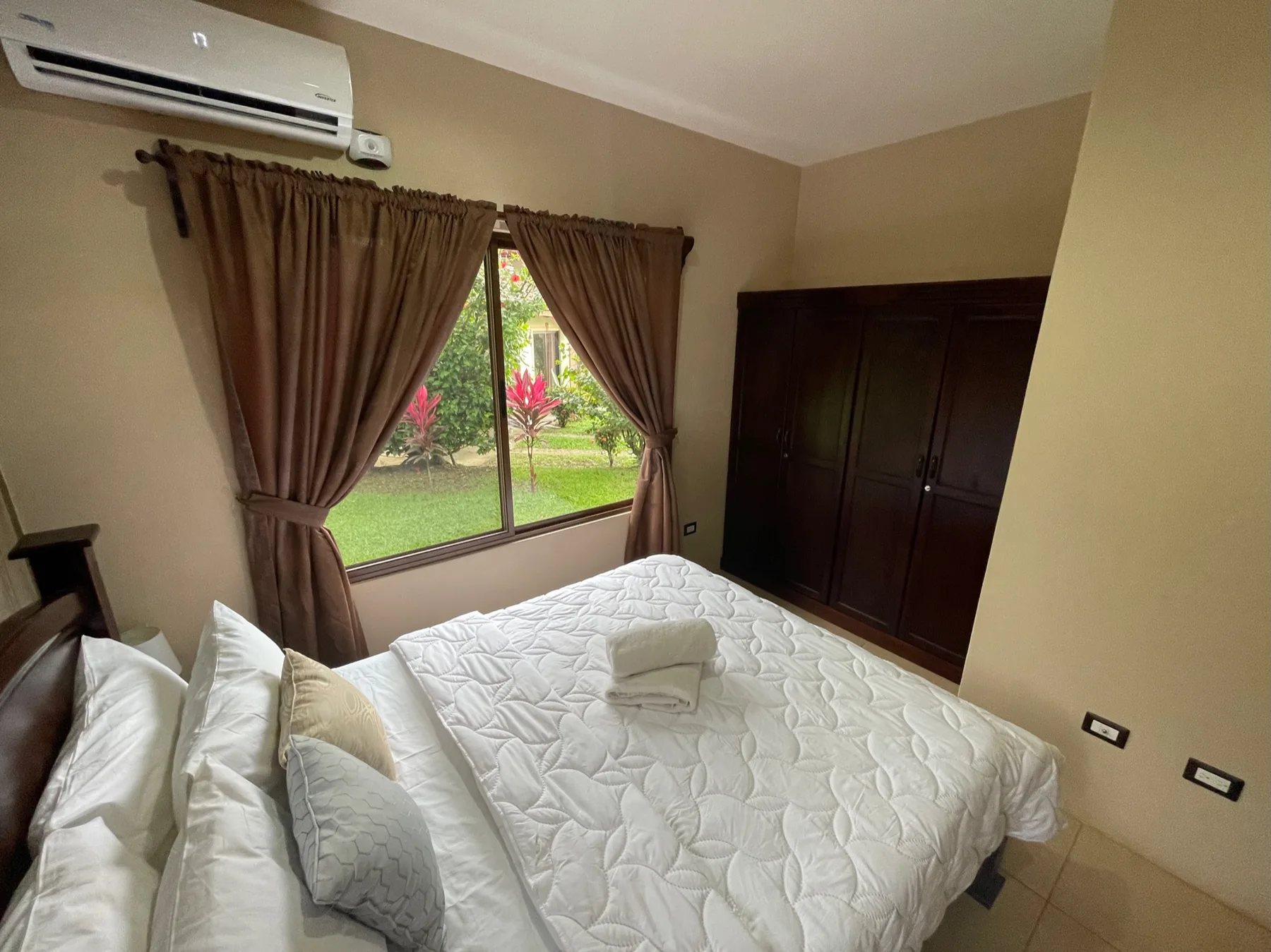 A bedroom with a bed beside a window overlooking a garden.