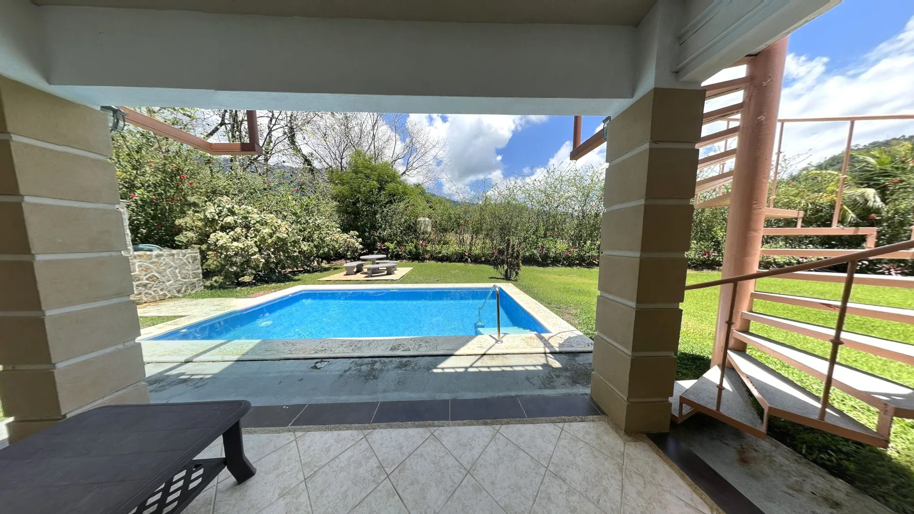 A covered patio overlooks a swimming pool and garden.