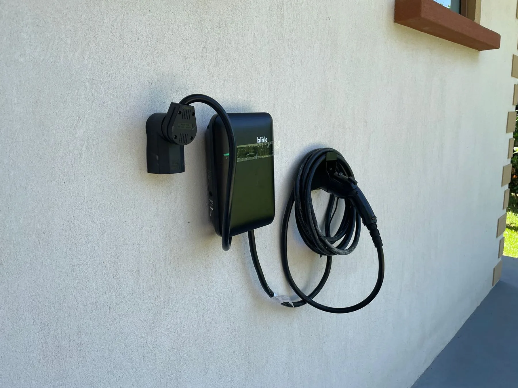 A wall-mounted electric vehicle charging unit with its cable coiled beside it.