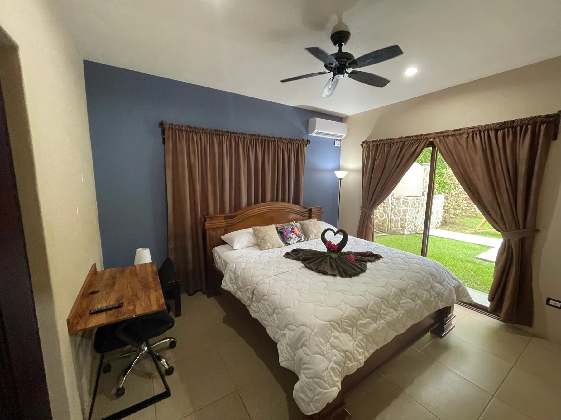 A bedroom with a bed, brown curtains, and a ceiling fan.