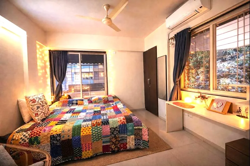 Un dormitorio con una colcha de retazos colorida y ventanas grandes.