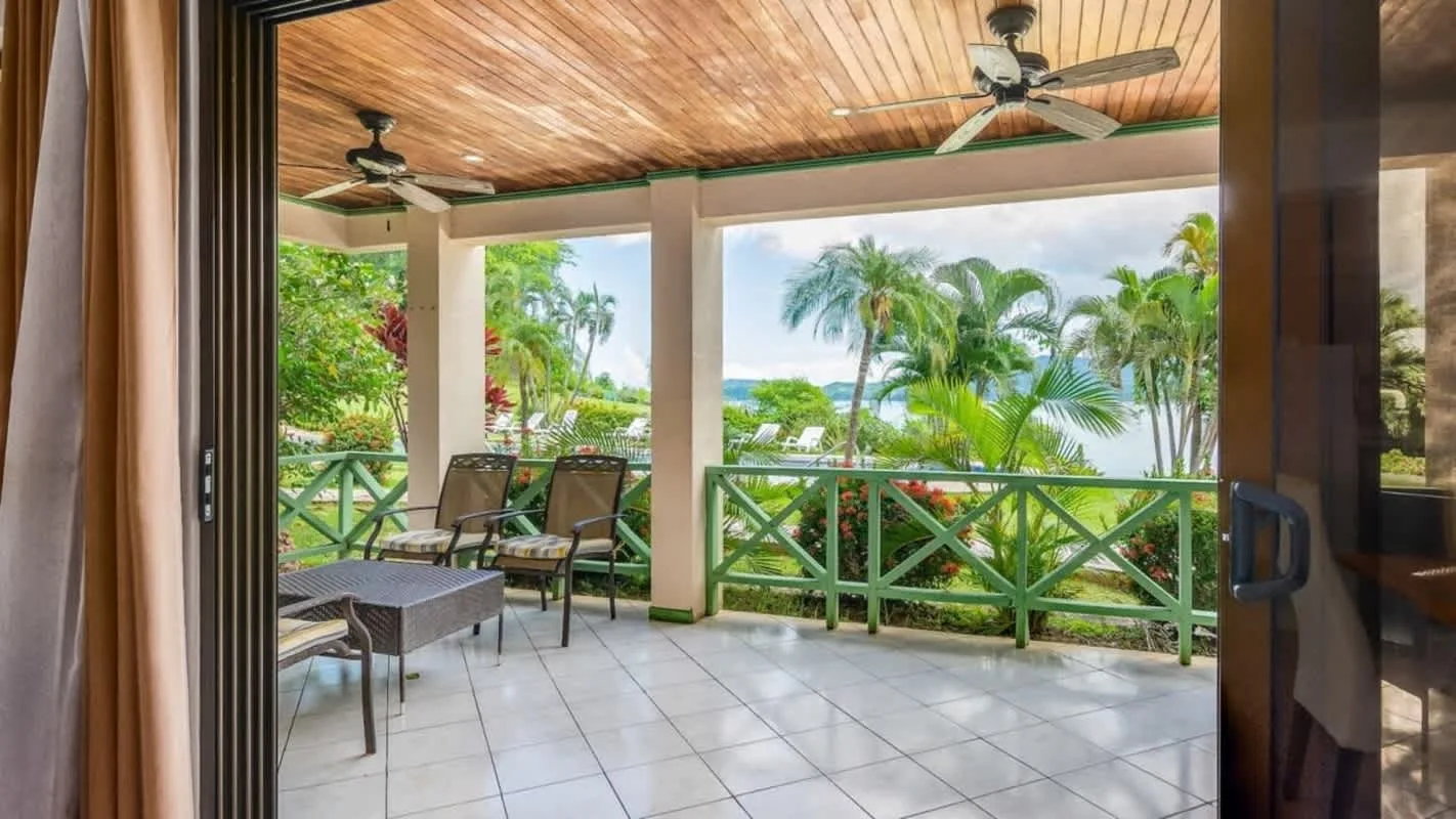 A covered patio with seating overlooks tropical greenery and the water.
