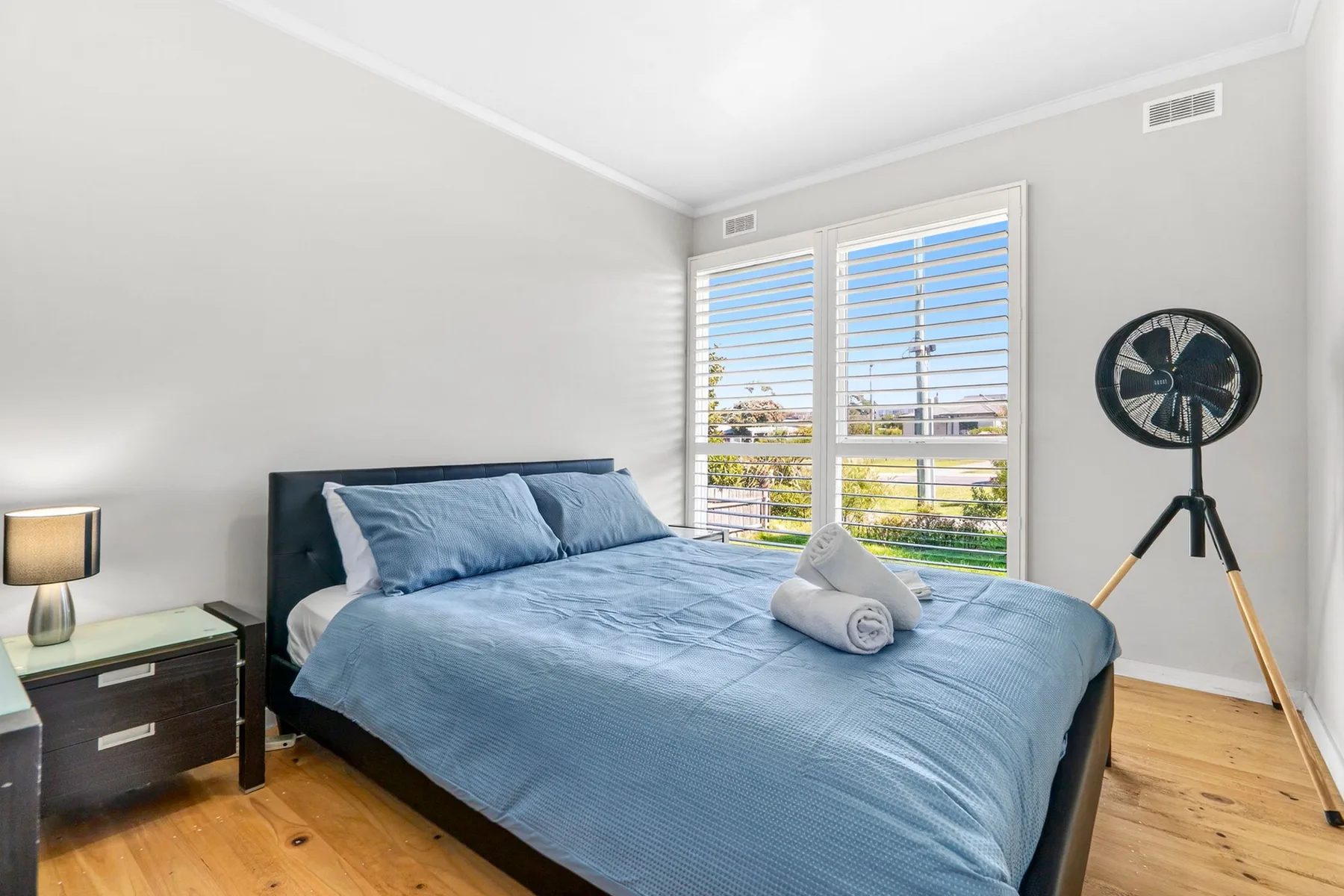 A bedroom with a blue bed beside a large window.