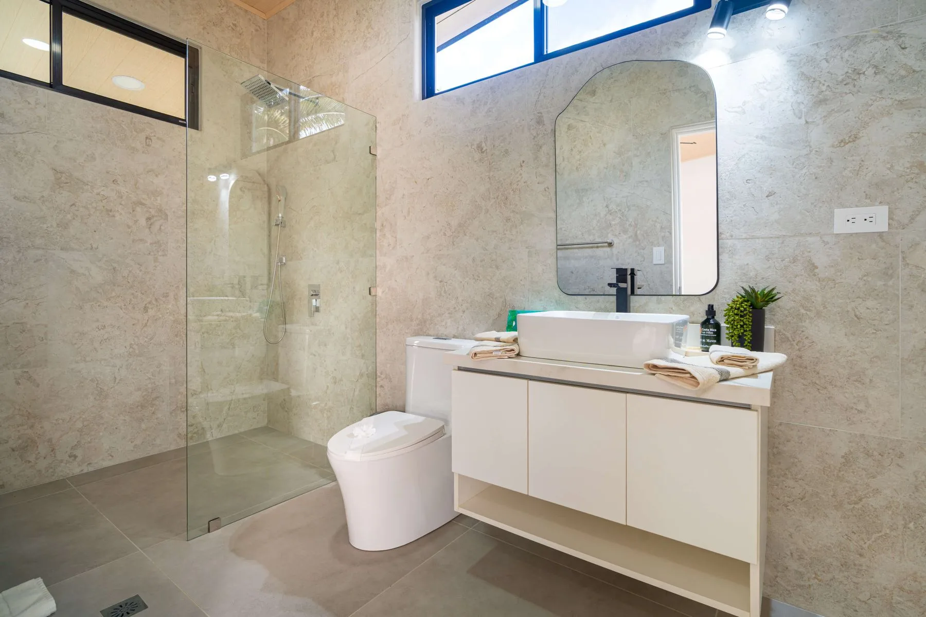 Baño luminoso con ducha de vidrio, inodoro y lavabo con mueble.