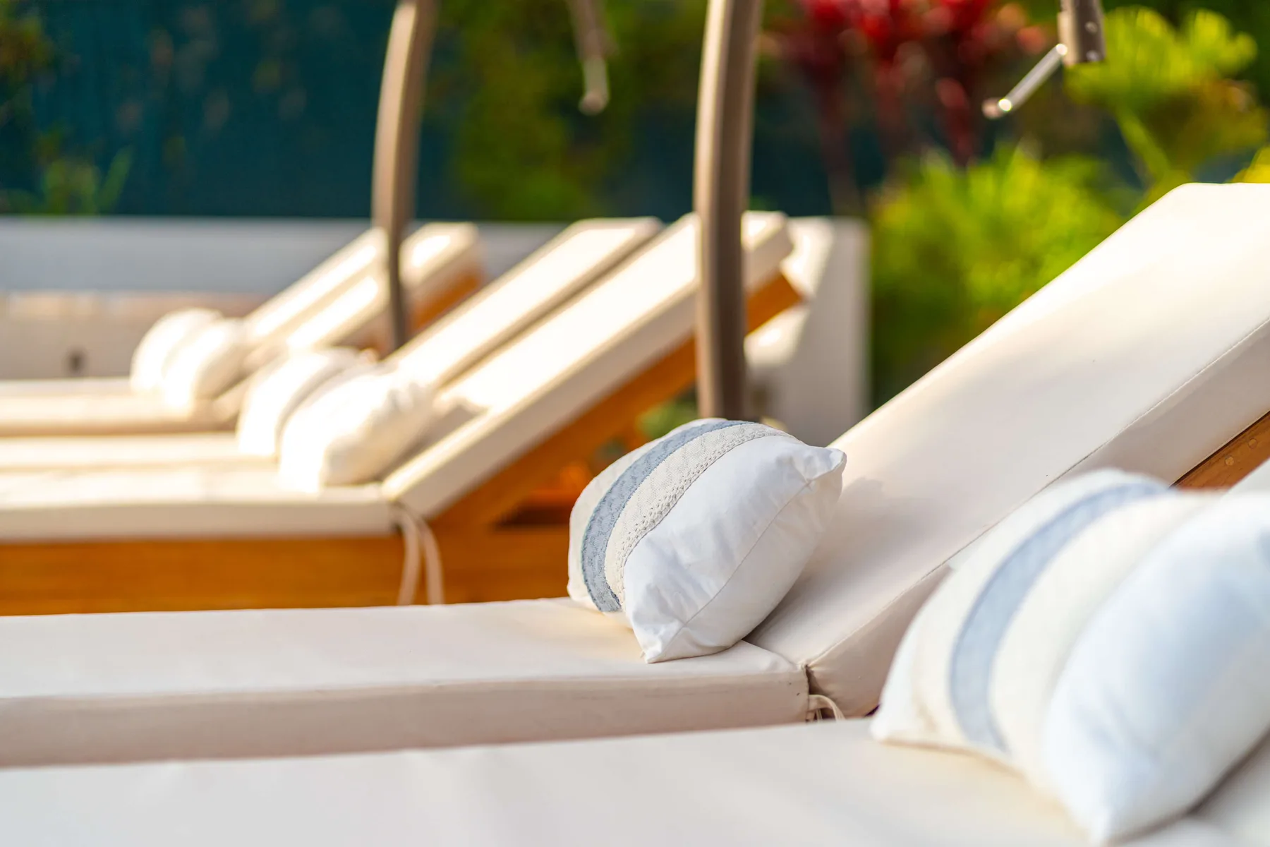 Tumbonas al aire libre con cojines claros junto a plantas verdes.