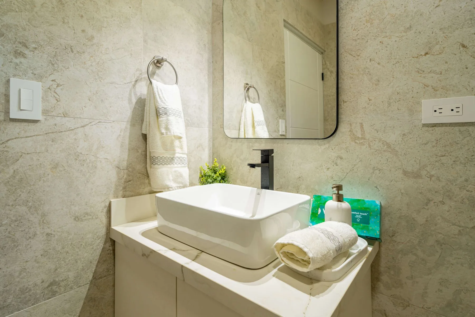 Un tocador de baño con lavabo sobre encimera, espejo y toallas dobladas.