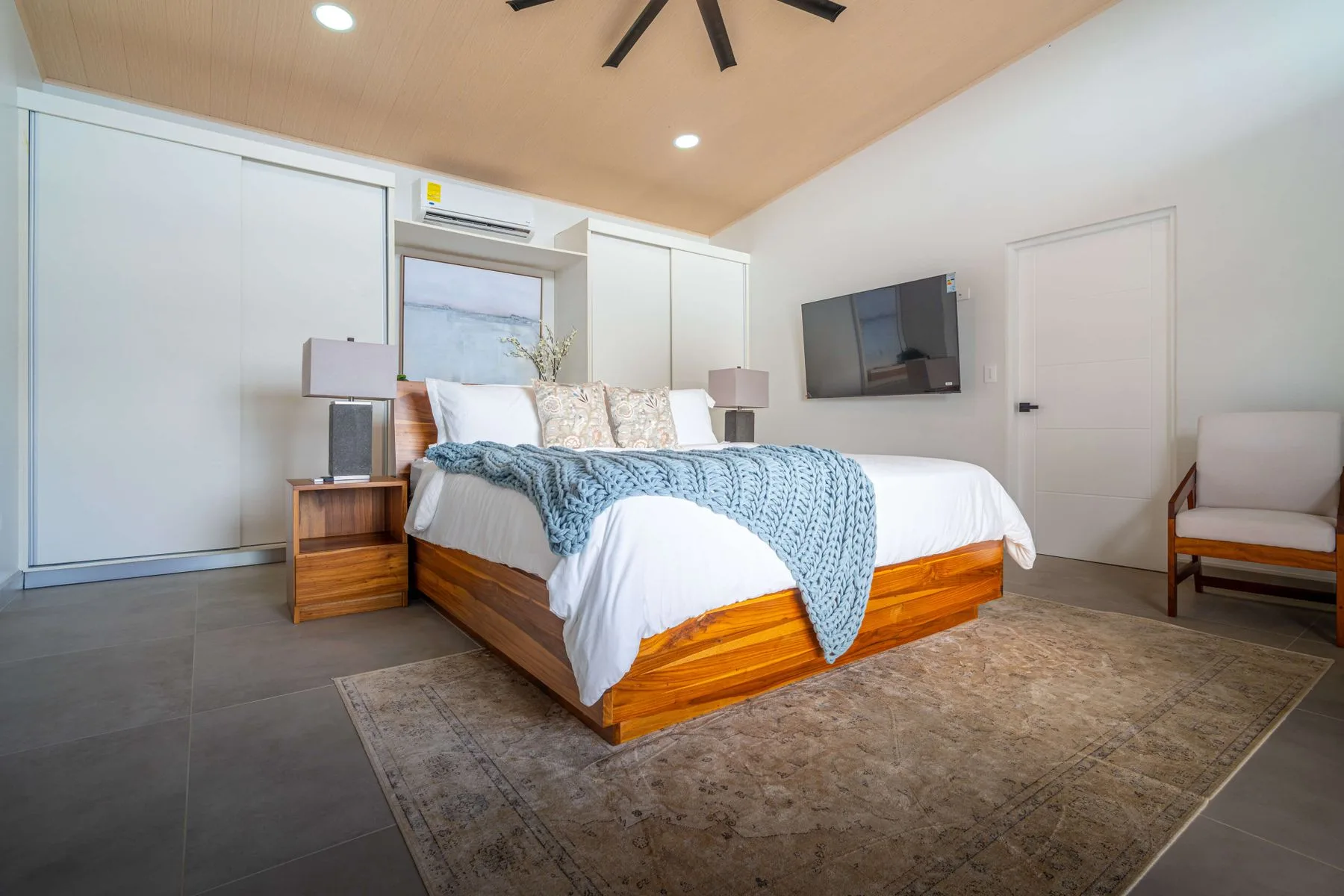 Dormitorio con una cama de madera, ropa de cama blanca y una manta azul.