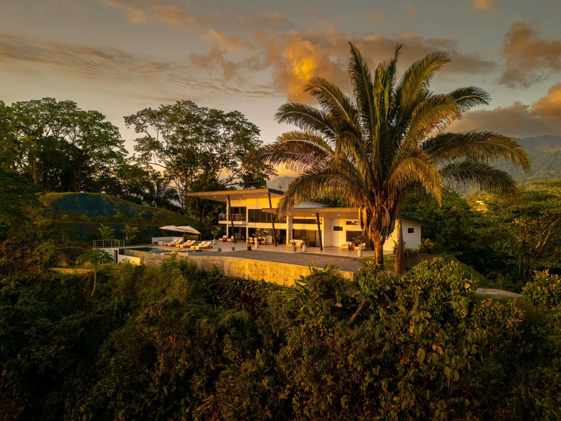 Una casa moderna está rodeada de árboles tropicales al atardecer.