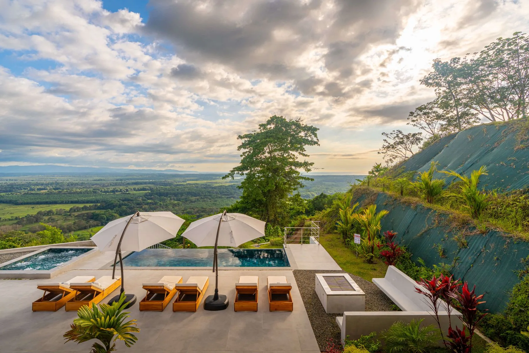 Una terraza con piscina al aire libre ofrece vistas a un amplio valle verde bajo un cielo nublado.