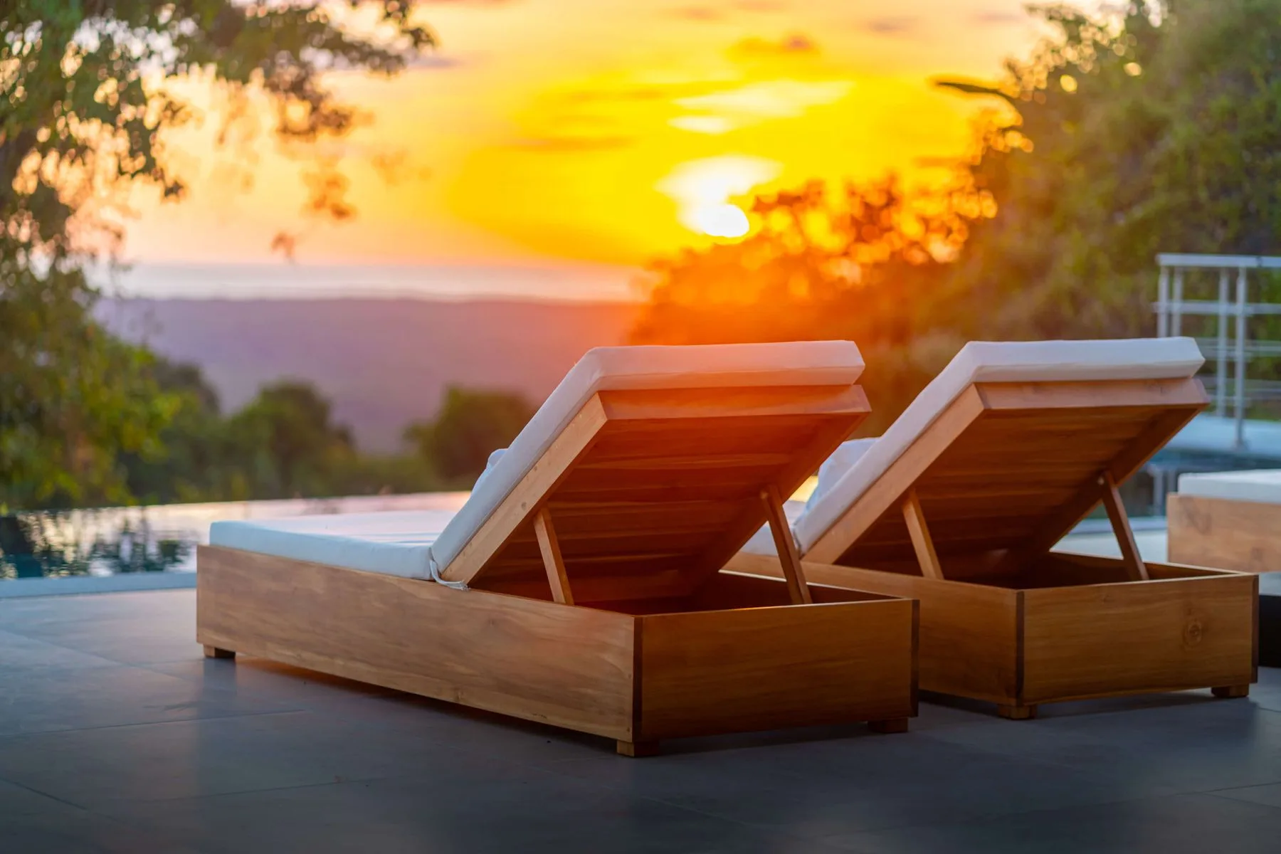 Dos asientos de madera junto a una piscina al atardecer.