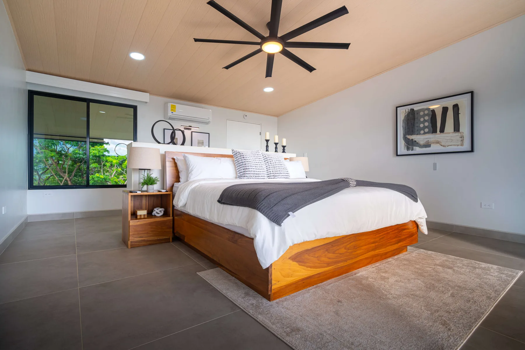Un dormitorio con una cama de madera, ropa de cama blanca y una ventana grande.