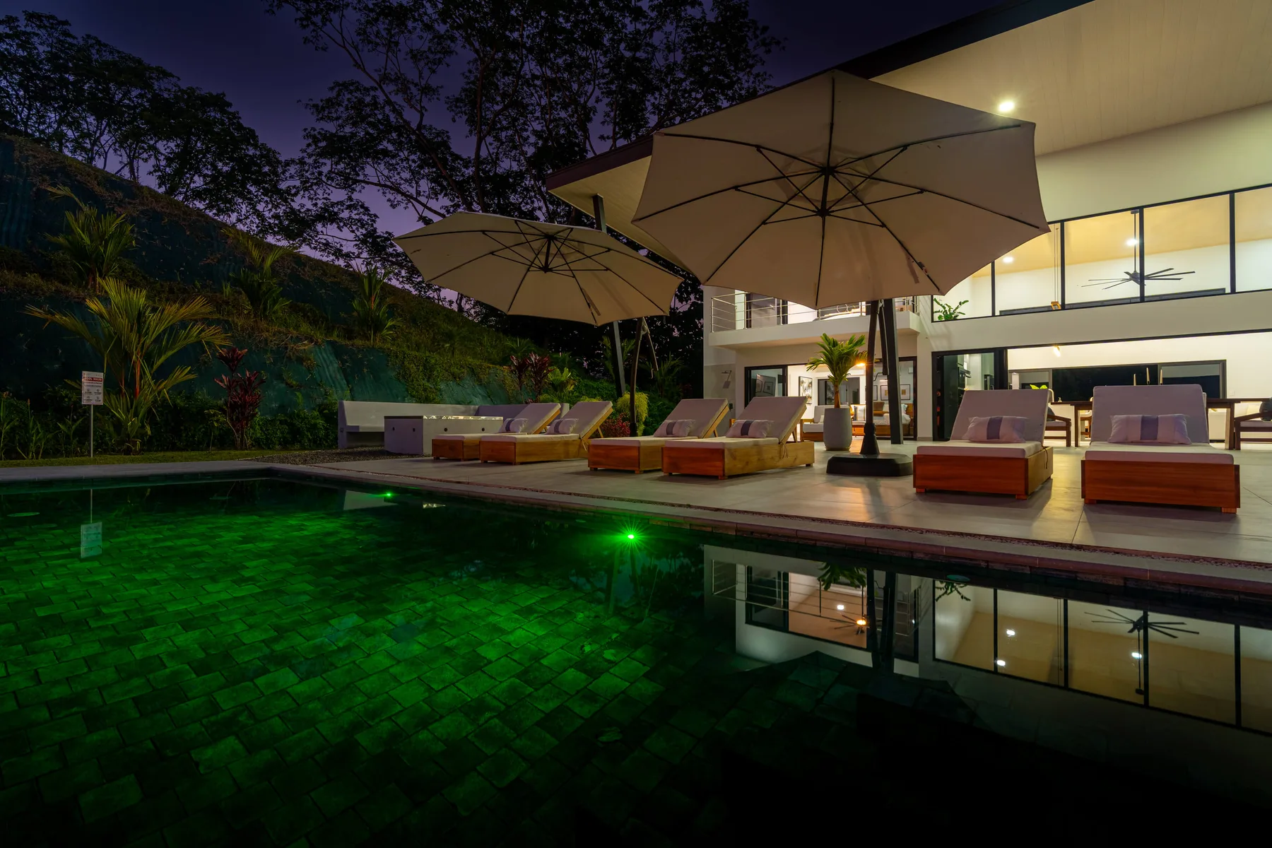 Una piscina de noche refleja el edificio y los asientos cercanos.