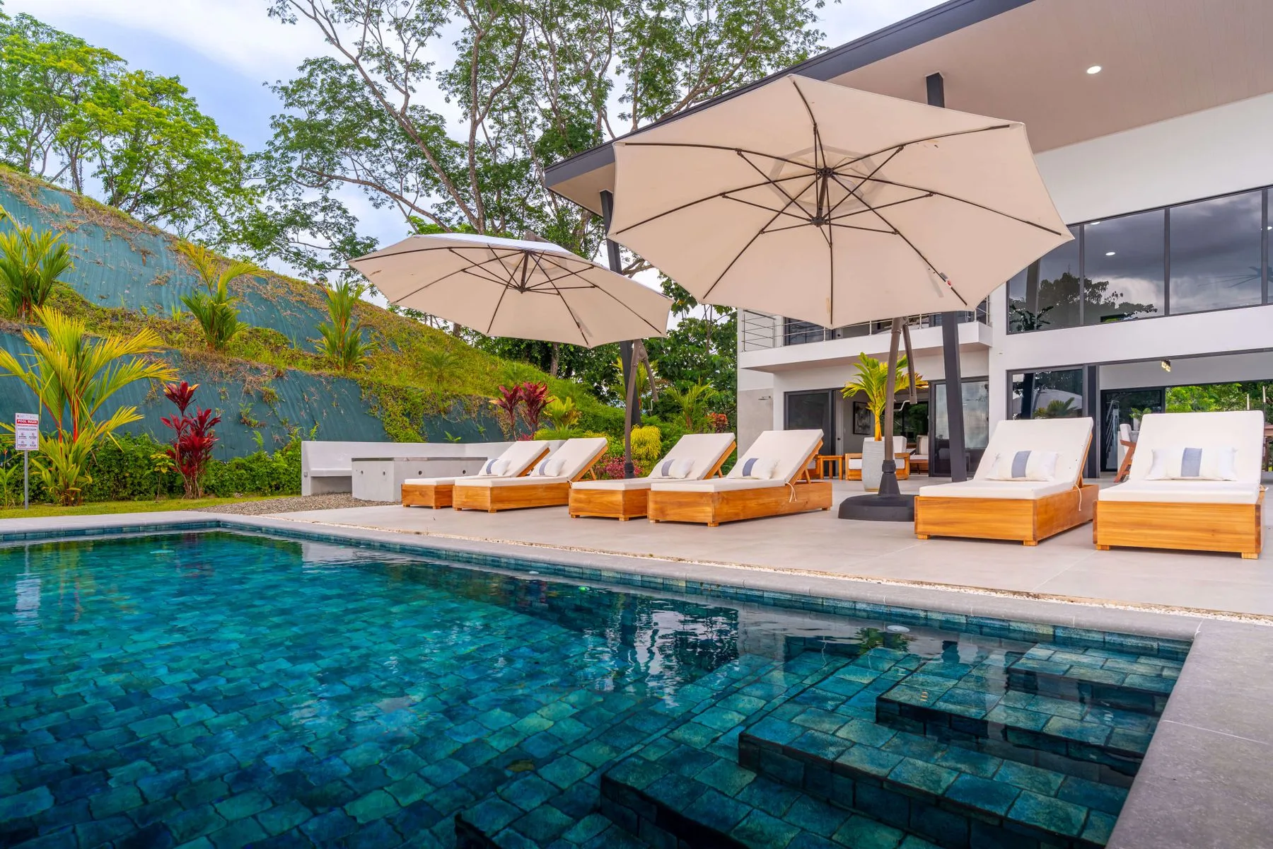 Una piscina al aire libre junto a asientos reclinables y grandes sombrillas.