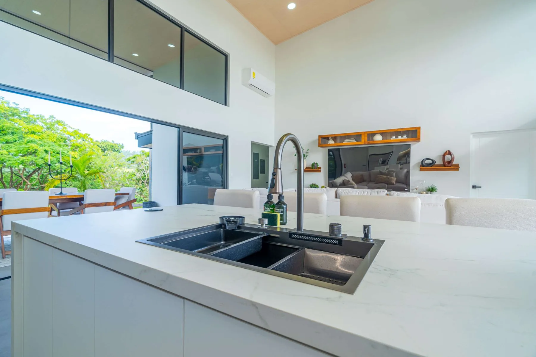 Una cocina moderna con una gran isla y fregadero da a una sala de estar y un patio.
