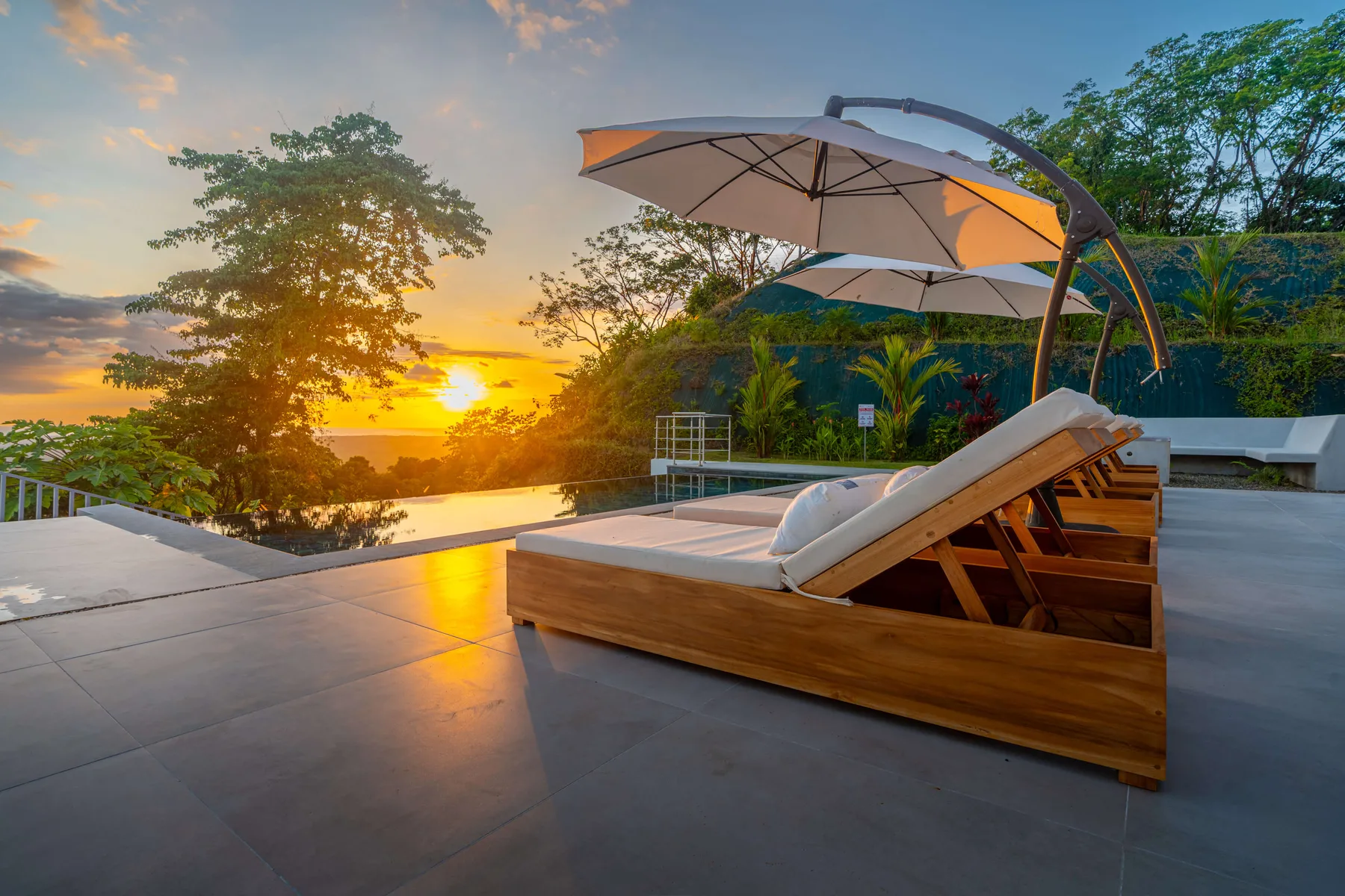 Asientos junto a una piscina al aire libre con sombrillas miran hacia el atardecer.