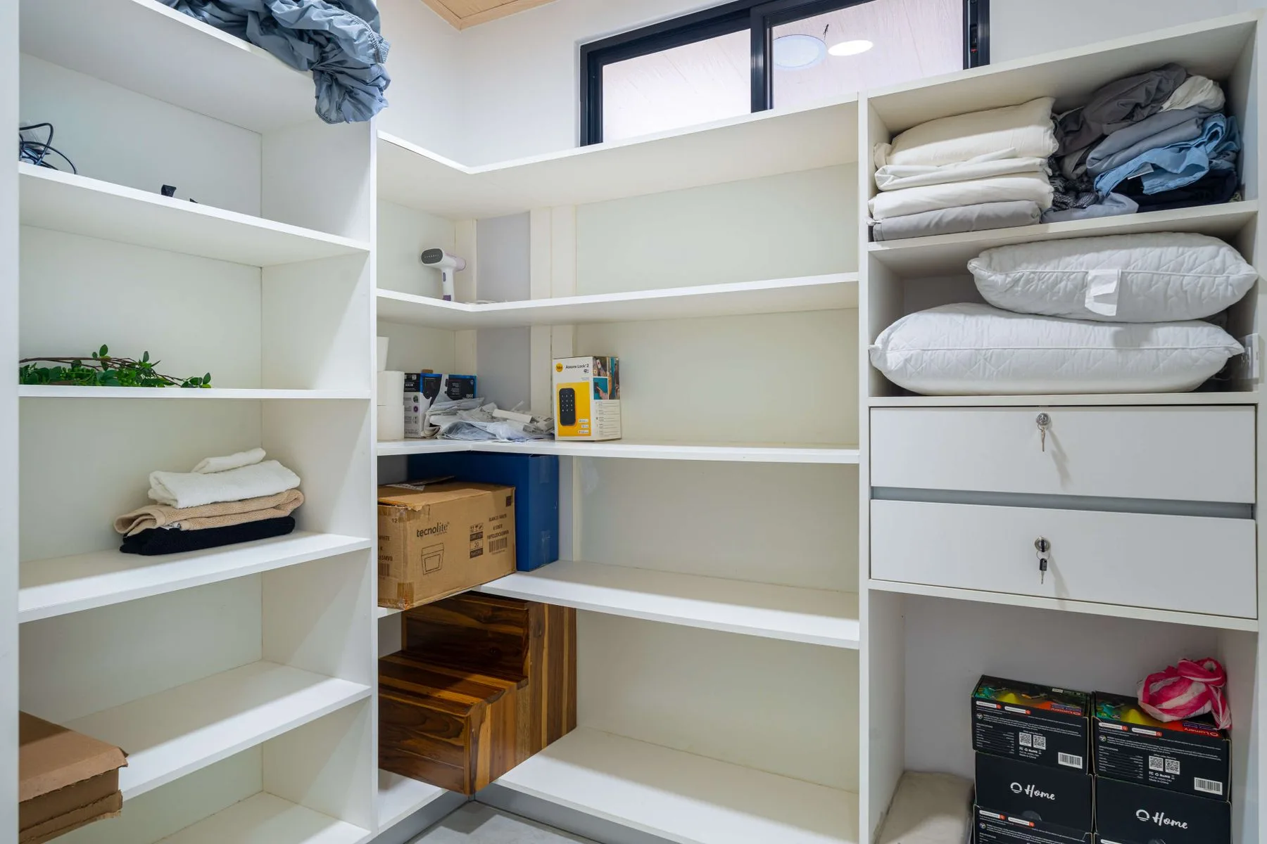 Un vestidor con estantes blancos, ropa de cama doblada y cajas de almacenamiento.