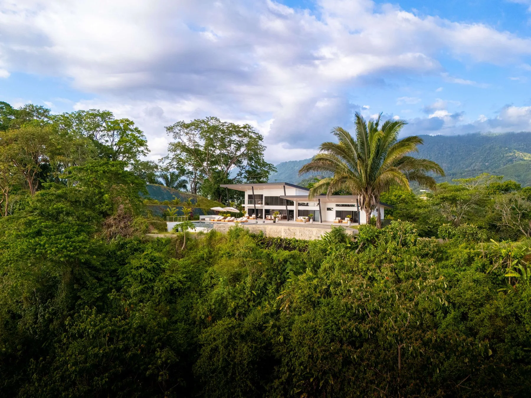 Un edificio moderno de poca altura está rodeado de vegetación, con montañas al fondo.