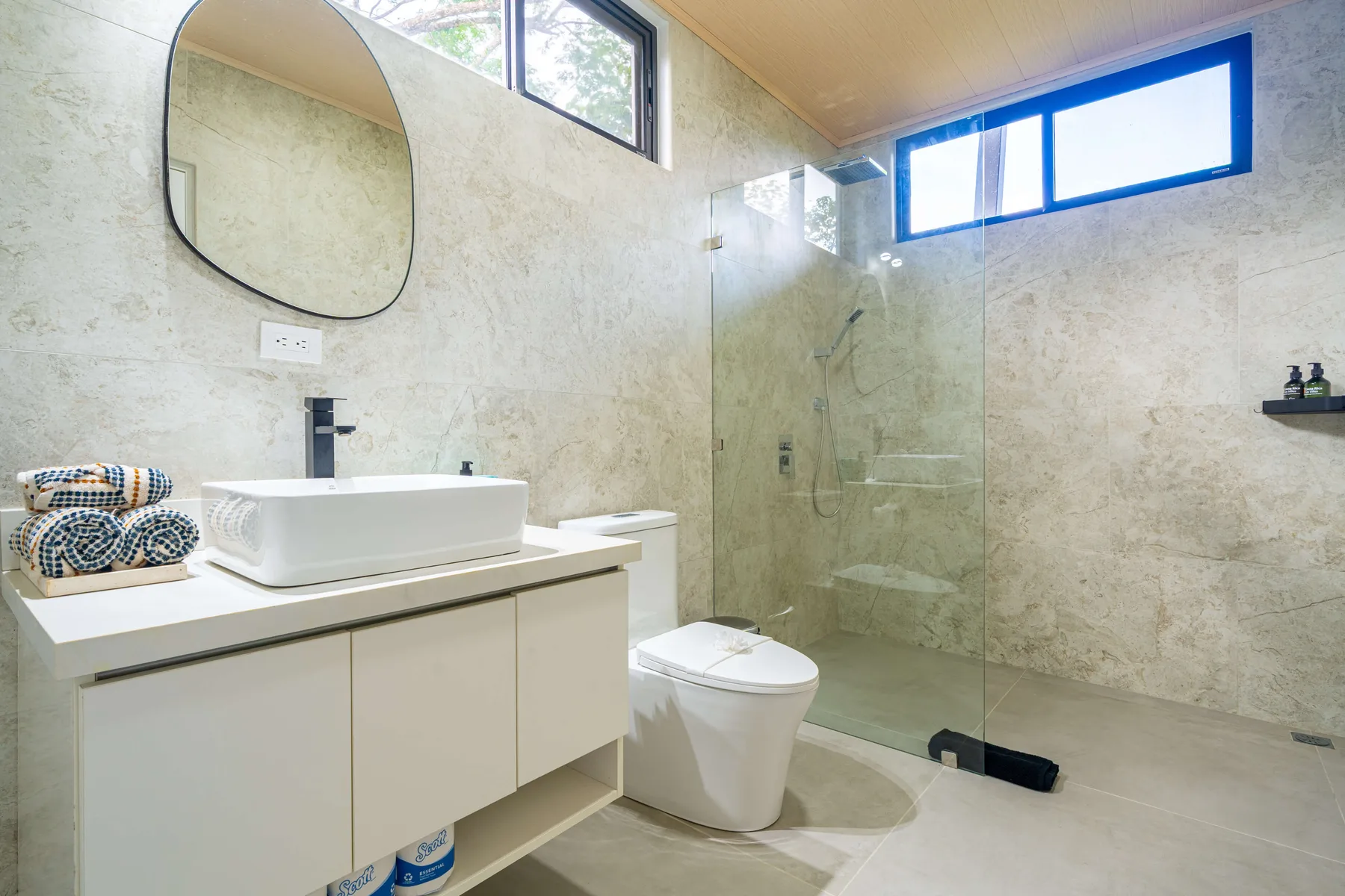 Un baño luminoso con lavabo, inodoro y ducha de vidrio.