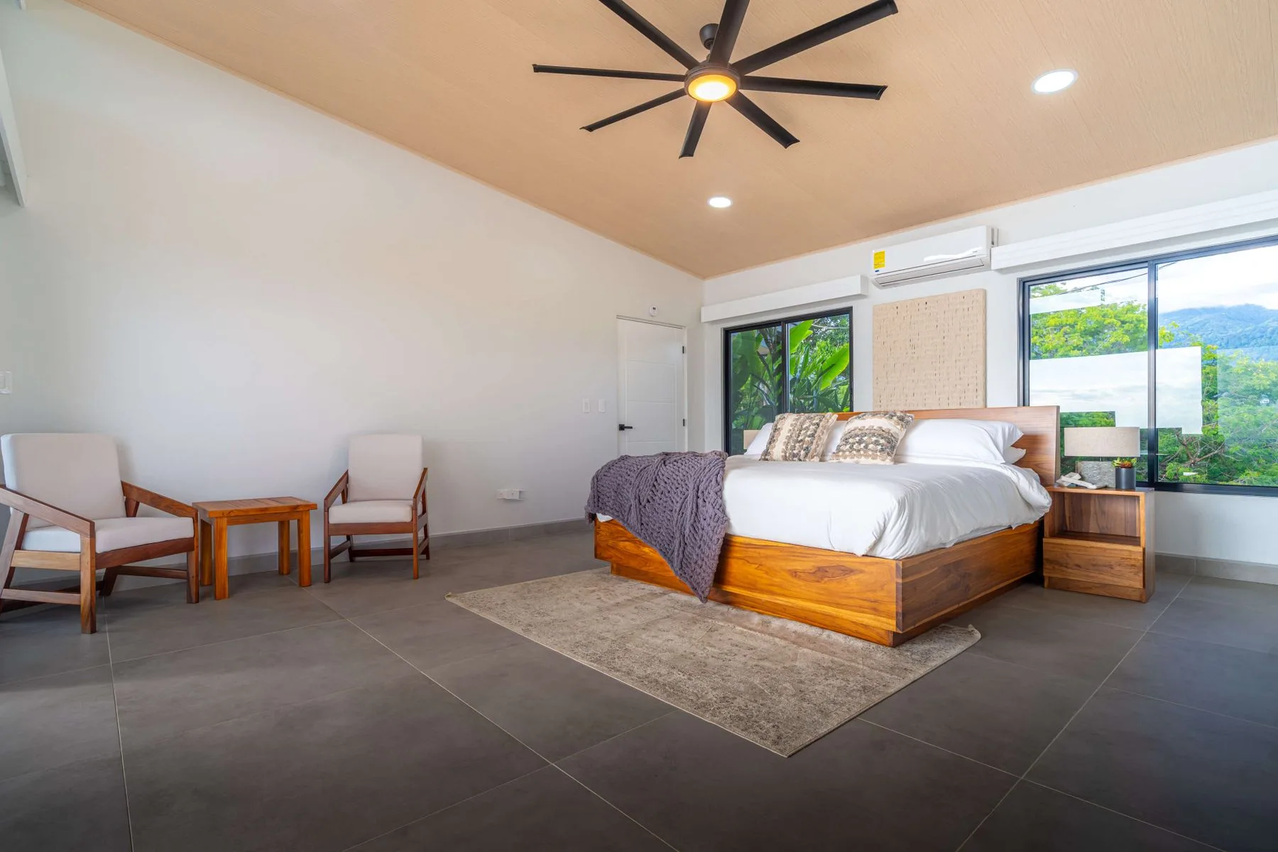 Dormitorio con una cama de madera, asientos y ventanas amplias.