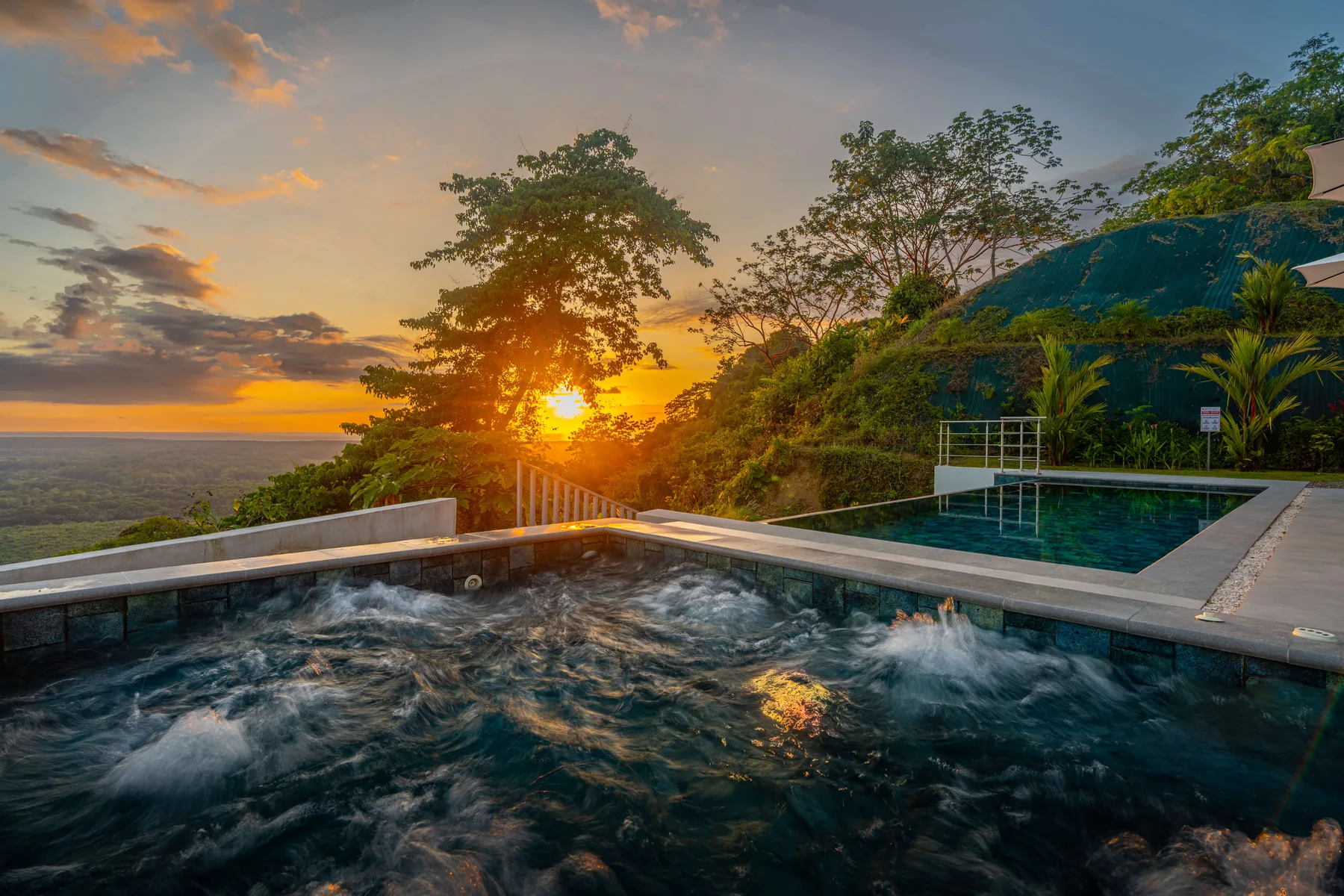 Una piscina al aire libre contempla el atardecer, con árboles y colinas en el horizonte.