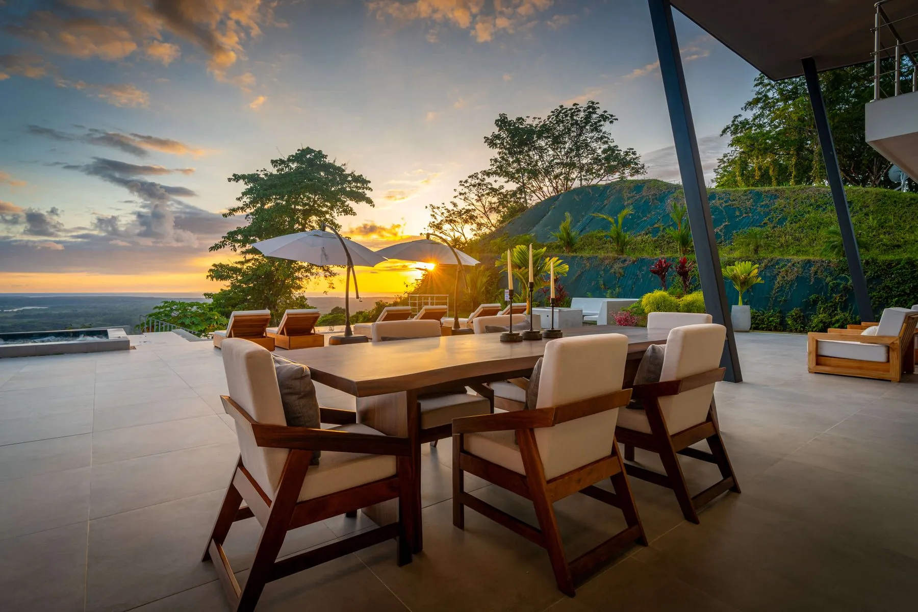 Un comedor al aire libre con mesa y sillas ofrece vistas de la costa al atardecer.