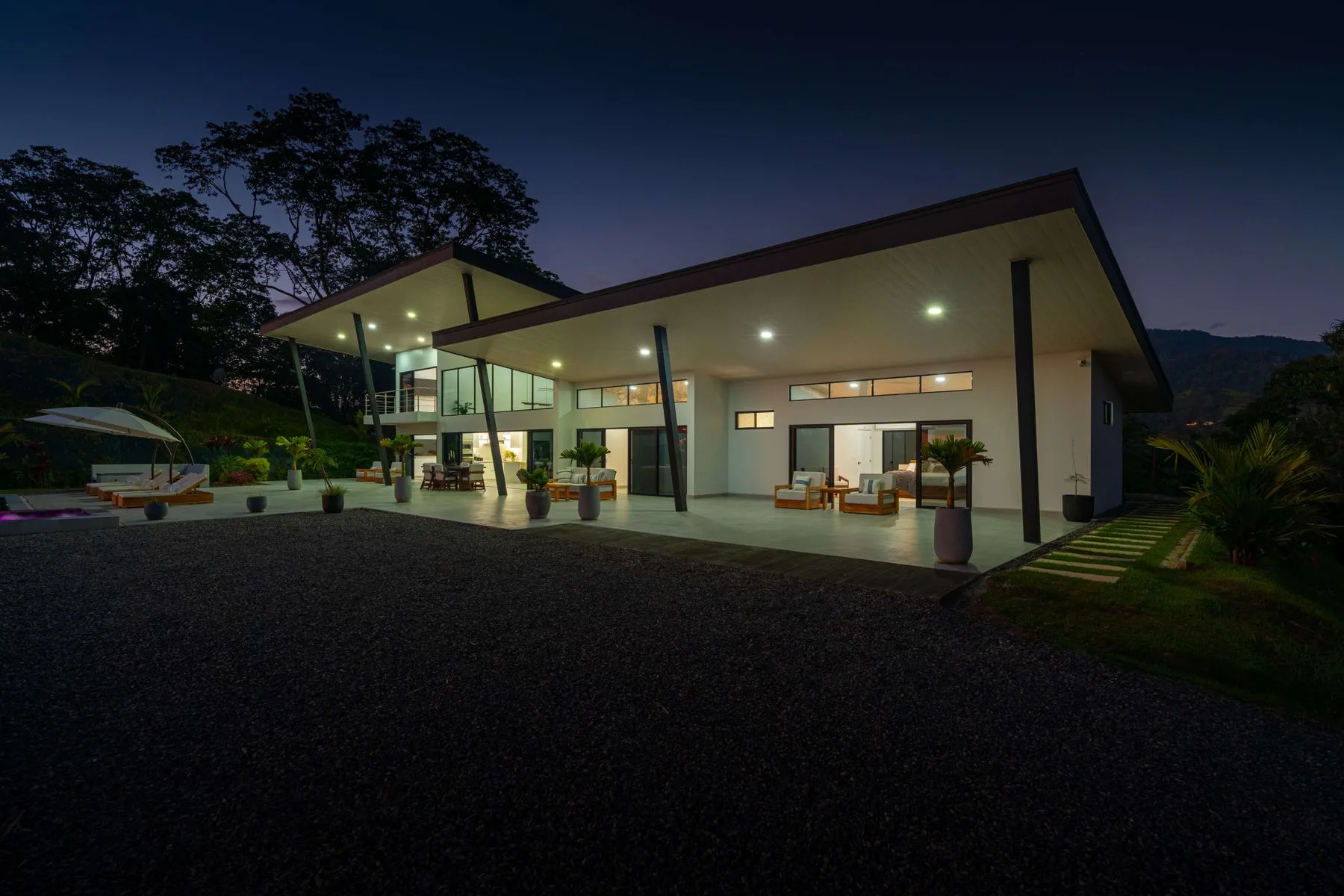 Una casa moderna resplandece al anochecer, con un patio cubierto y jardines.